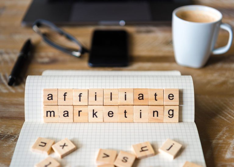 A desk with a computer, coffee mug, notebook, and letter tiles that spell out "affiliate marketing."