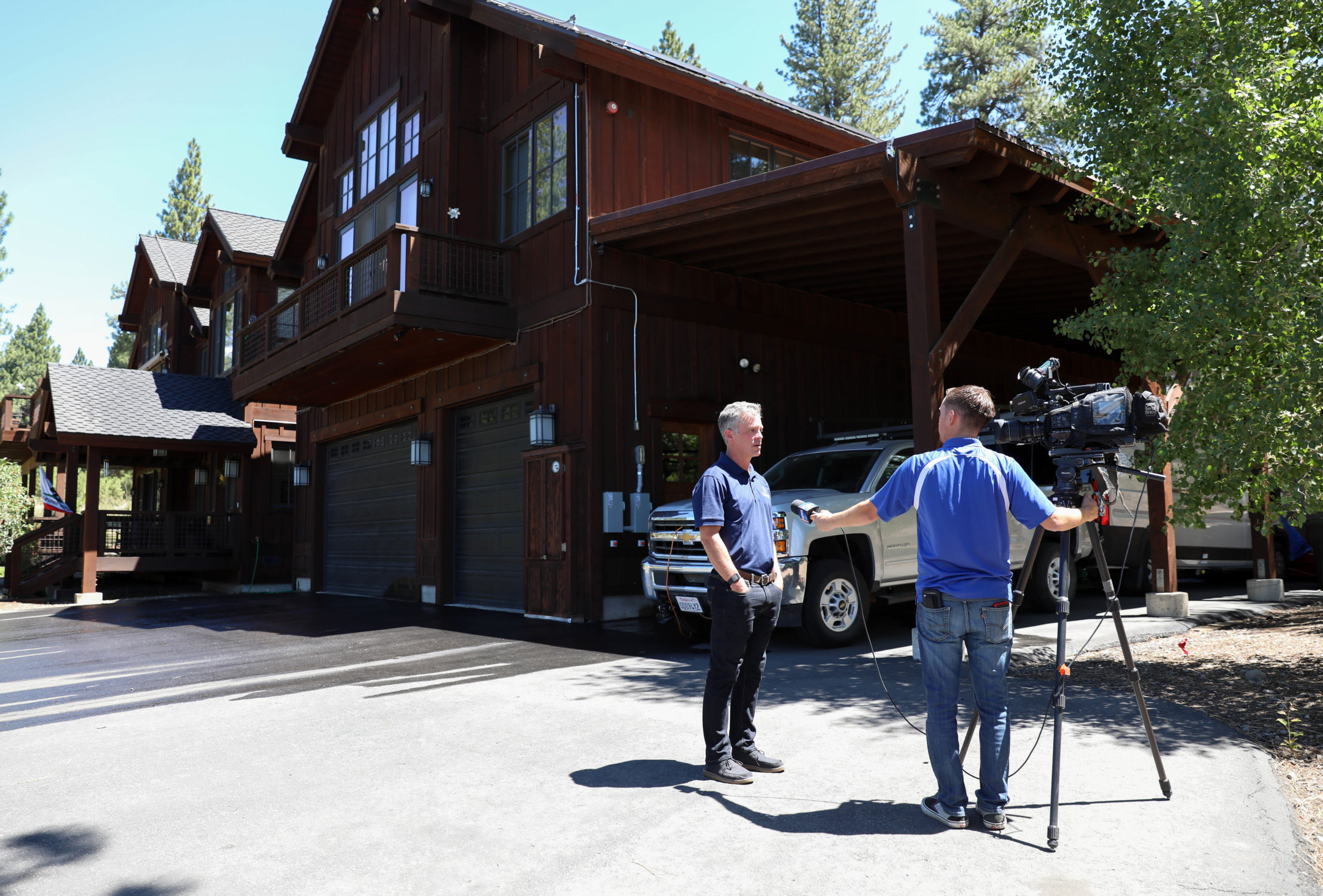 A man interviewing and video taping a man at a media event. They are standing in front of a home where a live demonstration of a digitally connected sprinkler system took place.