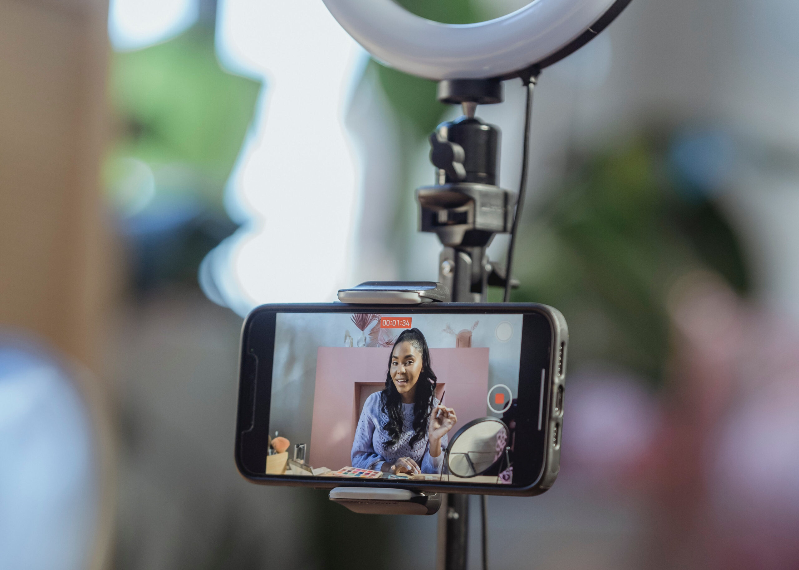 An image of a phone on a tri-pod with an influencer recording herself for social media on the phone screen.