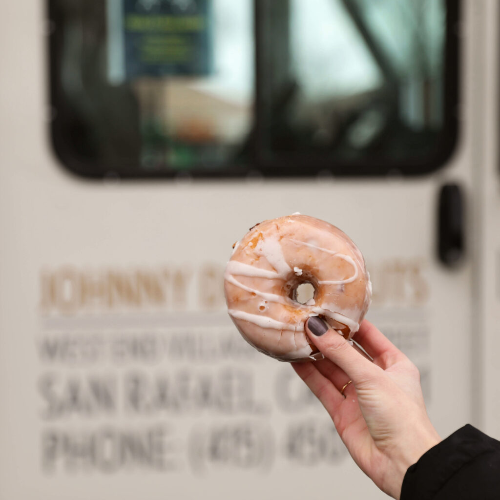 A food influencer holding a doughnut in front of a doughnut truck. 