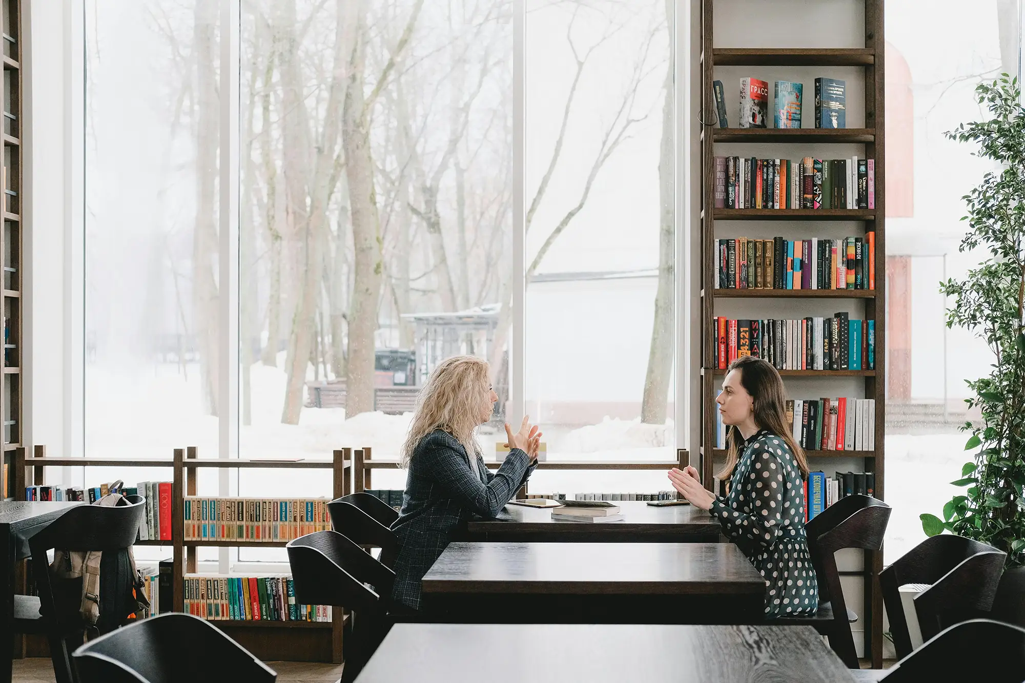 two women at a table in a library with snow outside the large window