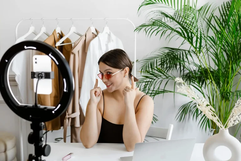 woman filming herself with ring light and cell phone showing off sunglasses