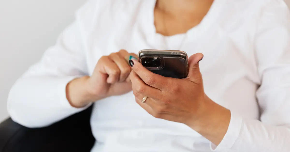 closeup of person in white shirt holding and engaging with their mobile phone