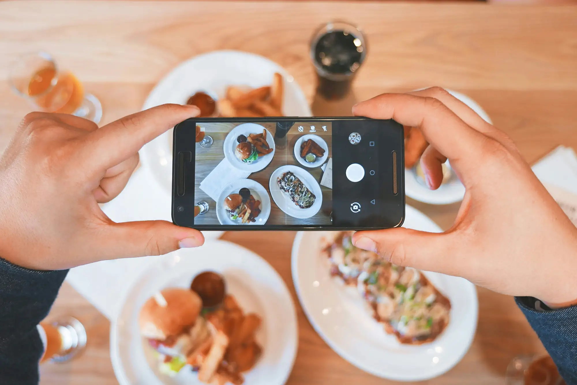 hands holding a phone taking a photo of a table full of food